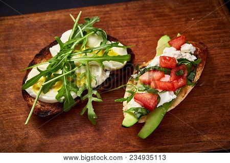 Grilled Toast Brisket With Tomato, Avocado And Ruccola On Wooden Cutting Board Over Dark Background,