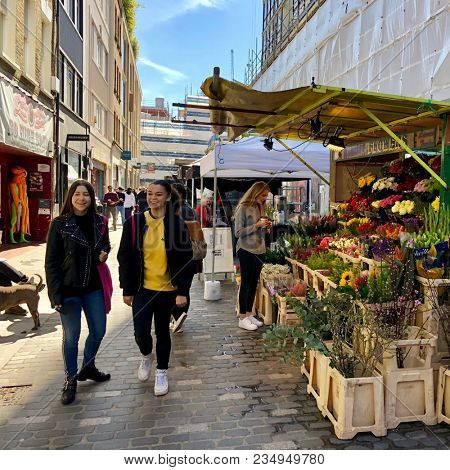 SOHO, LONDON - APRIL 5, 2018: Pedestrians at a market selling food, flowers, fruit and vegetables on Berwick Street in Soho, London, UK.