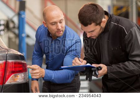 auto service, repair, maintenance and people concept - mechanic with clipboard and customer or car owner looking at taillight at workshop