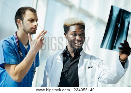 Two Doctors Holding And Analysing An Xray In A Bright Modern Office Office. Multi Ethnic Doctors Dis