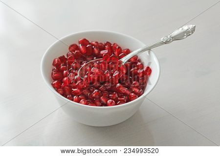 Grains Of Red Ripe Pomegranate Lie In A White Bowl With A Spoon. Big Ripe Red Granets Or Garnets. Fr