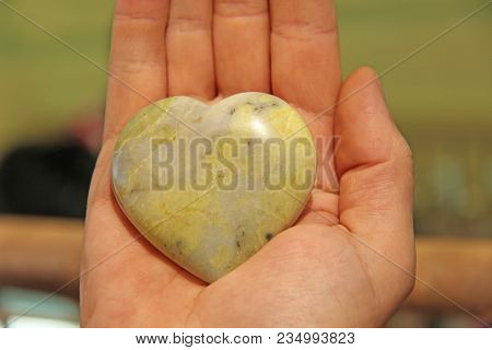 The Hand Holds A Heart Made Of Natural Stone Yellow Jadeite. Heart In Hand. A Stone In The Shape Of 