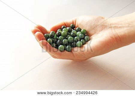Natural Green Jade Nephrite Mineral Stones Beads. The Green Jade Stone Lies In The Hands. Hands Hold