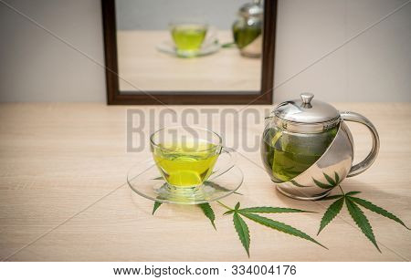 A Glass Of Hot Marijuana Tea And Tea Pot On The Table . Cannabis Concept.