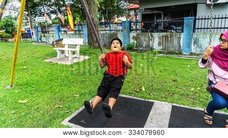 Young Kid Playing With The Swing Happily With His Sister At The Playground In Paya Jaras.