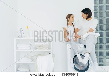 Caring Mother Talks With Daughter, Pose On Washing Machine, Surrounded With White Linen, Do Washing 