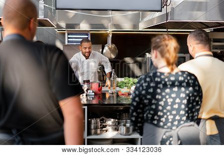 In Focus Is The Chef Who Conducts A Master Class In Cooking. In The Foreground Are Blurred Images Of
