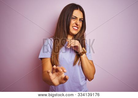 Young beautiful woman wearing casual t-shirt standing over isolated pink background disgusted expression, displeased and fearful doing disgust face because aversion reaction. With hands raised. Annoy