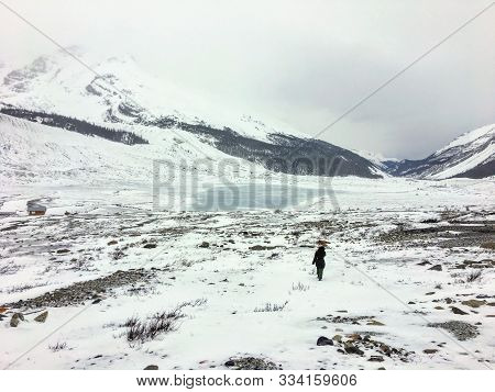 A Distant Faraway View Of A Female Hiker Alone Walking Through The Vast Winter Landscape Towards The