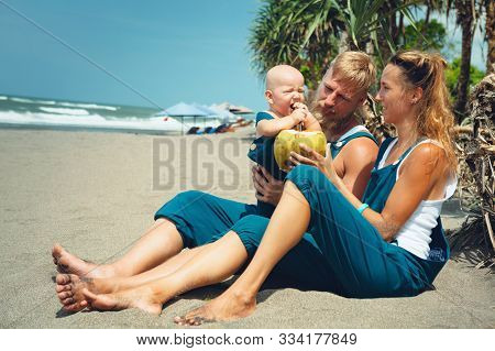 Happy Hipster Family Funny Picnic On Beach - Mother, Father Feed Baby Boy. Little Son Eat Fruits Wit