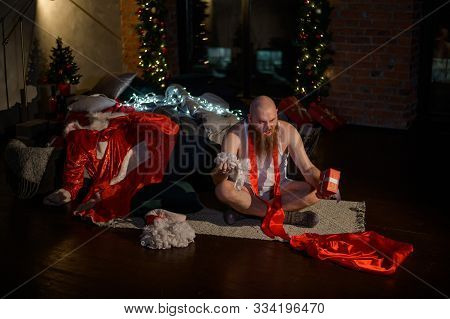 Bad Santa Claus On The Background Of Christmas Decorations. A Man In A Suit Of Santa Claus After The