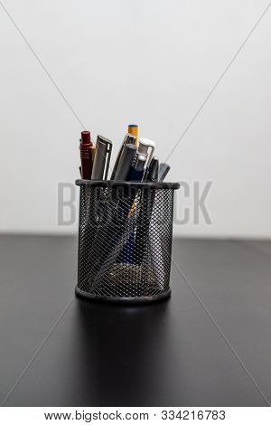 Black Office Pot With Pencils And Pens On A White Background. Metal Pen Pot On Black Desk.