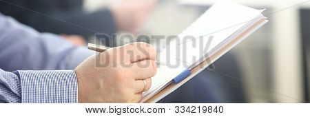 Focus On Male Hand Writing Something. Businessman Sitting In Modern Conference Room And Holding Pape