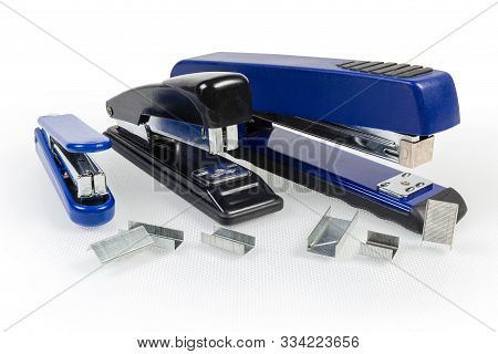 Paper Manual Hand-held Staplers Different Sizes And Expendable Metal Staples To Them On A Light Surf