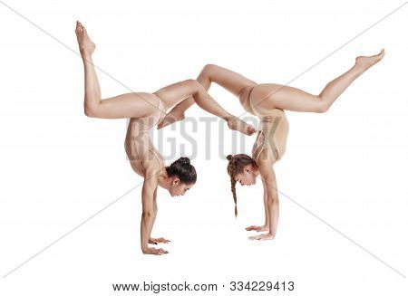 Two Flexible Girls Gymnasts In Beige Leotards Performing Complex Elements Of Gymnastics Using Suppor