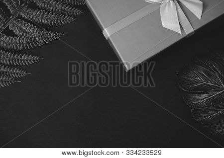 A Gift Box And Leaves Of Fern And Monstera On Dark Background Flat Lay Top View