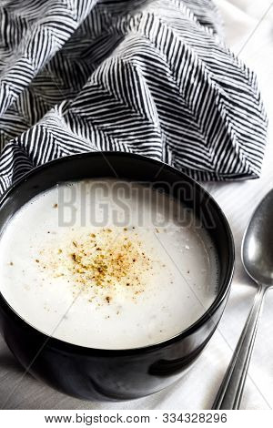 Cauliflower Soup (creme Du Barry) In Black Bowl On White Background With Black And White Cloth