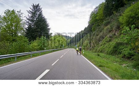 A Highway Through A Forest With Turns And Two Cyclist Riders Ride Along It. Schwarzwald Forest Road 