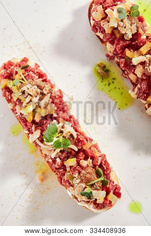 Exquisite serving beef tartare on toast with pickles and black garlic cream on white restaurant plate isolated. High cuisine restaurent dish, minced veal steak meat in minimalist style