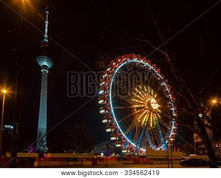 Berlin, Germany - December 12, 2018: Illuminated Ferris Wheel at Christkindlmarkt (Christmas market) in Central Berlin. Fernsehturm Television Tower is seen in background