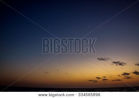 Sunset Over The Sea. In The Night Sky A New Moon. The Horizon Line Has A Curvature In The Compositio