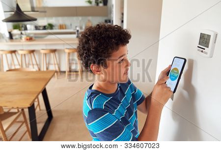 Boy Changes Temperature On Central Heating Thermostat Control Using Mobile Phone App