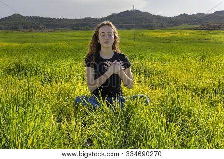 Young Caucasian Woman Red-haired With Freckles, Resting On A Green Field At Spring Sunset, Sitting I
