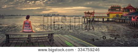 Tourist sitting at Yeoh jetty at sunrise, Georgetown, Penang, Malaysia. Panorama