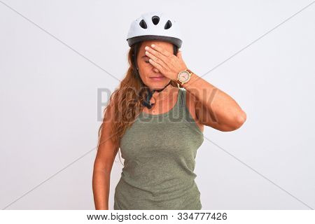 Middle age mature cyclist woman wearing safety helmet over isolated background covering eyes with hand, looking serious and sad. Sightless, hiding and rejection concept