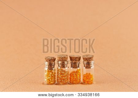 Yellow And Red Beads In Glass Jars On Bright Orange Background. Beads In A Transparent Container Wit