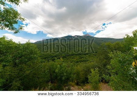 Green valley in front of the mountain. Impenetrable thickets of forests. Peak mountain in the clouds. The blue sky. Beautiful daytime landscape.