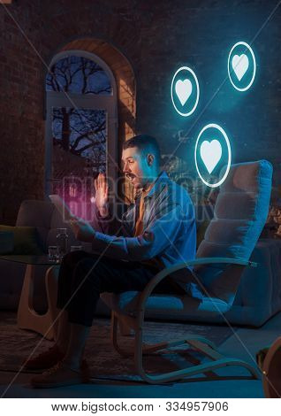 Insomnious Man Using Gadget With Neon Notifications At Home At Night. Sitting On Armchair, Flirting,