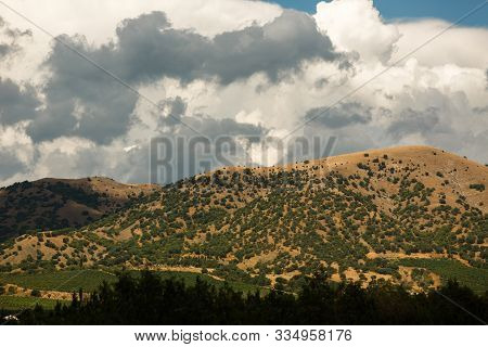 The peak of the mountain goes high into the sky. White clouds on a blue sky. At the foot of the mountain is a valley and a green forest. The tourism industry, a place to relax in nature.