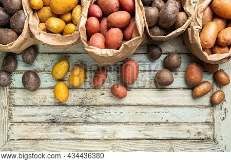 Various Varieties Of New Raw Colorful, White, Red And Purple Potatoes In Paper Bags On White Wooden 