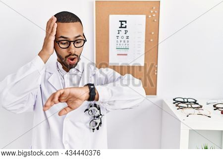 African american optician man standing by eyesight test looking at the watch time worried, afraid of getting late 