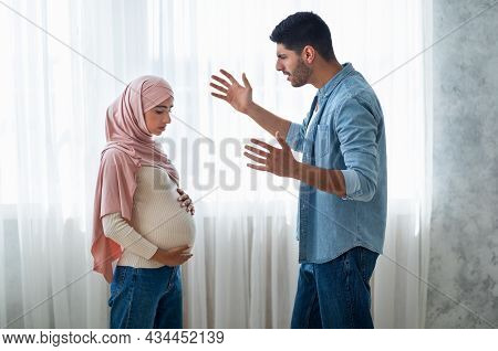 Angry Arab Man Shouting At His Pregnant Muslim Wife, Standing Near Windiw At Home, Side View