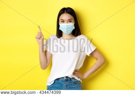 Covid, Health Care And Pandemic Concept. Asian Female Model In Medical Mask And White T-shirt Pointi