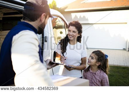 Delivery Man Delivering Parcels To Beautiful Woman And Her Daughter In Front Of The House.