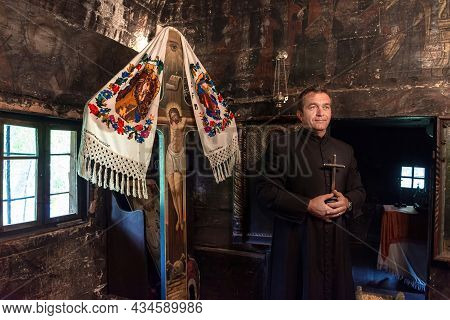 Salaj, Romania-may 16, 2018: Orthodox Priest Holding A Christian Cross, Praying In A Old Wooden Chur