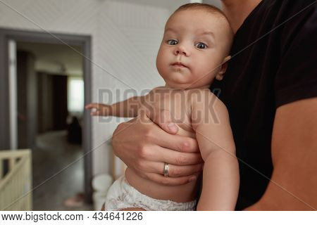 Portrait Of Funny Surprised Baby Held By Unrecognised Male Hands. Unrecognisable Man In Black T-shir