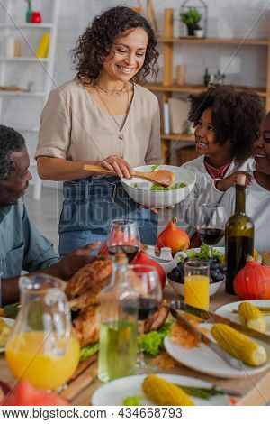 African American Mother Holding Salad Near Smiling Family And Thanksgiving Ginner