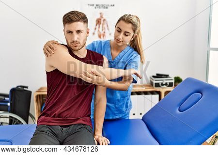 Young hispanic physioterapist woman make arm rehab treatment to man at the clinic.