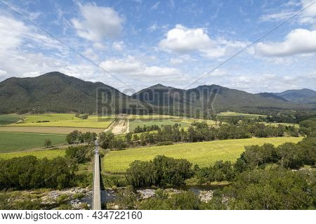 Bridge Over A Rocky Creek Amongst Fields Of Sugarcane And A Mountain Background Under A Cloudy Blue 