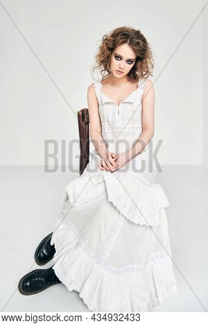 Portrait Of Attractive Strange Sad Girl. Beautiful Odd Young Woman In White Dress Sitting On Chair I
