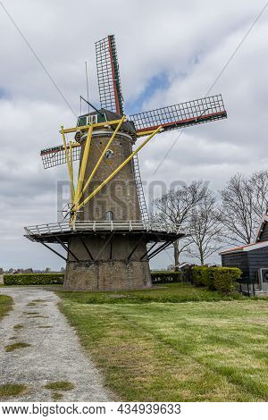 Korenbloem Windmill With Its Yellow Start Bars, Blades Next To A Path Between Grass, Stormy Sky In T