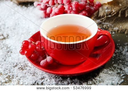 Still life with viburnum  tea in cup, berries and snow, on  wooden background