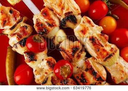 fresh grilled chicken shish kebab served wtih tomato cherry hot peppers on skewers over red plate isolated on white background