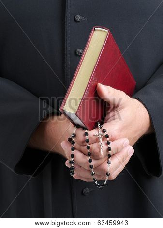 Closeup of catholic priest's hands holding the Holy Bible and rosary
