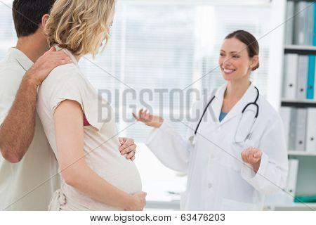 Beautiful female gynaecologist welcoming expectant couple in clinic