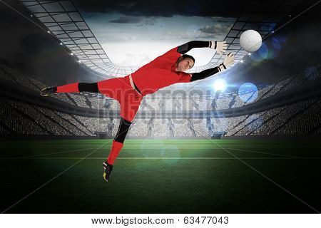Fit goal keeper jumping up in a large football stadium with lights